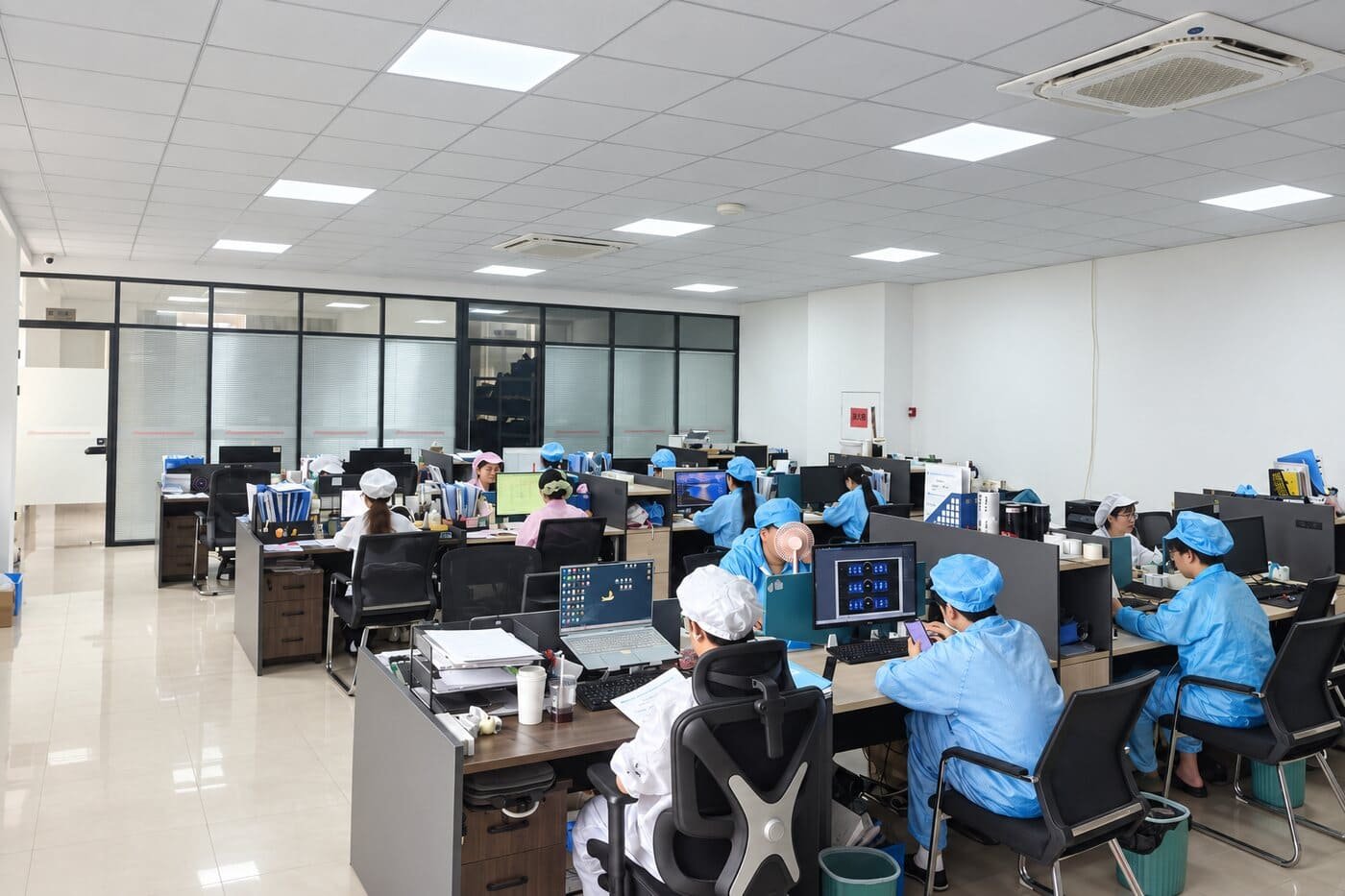Open engineering office where staff work in cleanroom gowns and caps